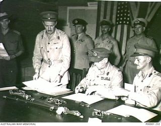 THE SOLOMON ISLANDS, 1945-09-08. LIEUTENANT GENERAL SIR STANLEY G. SAVIGE (GENERAL OFFICER COMMANDING II AUSTRALIAN CORPS) ADDS HIS SIGNATURE TO THE INSTRUMENT OF SURRENDER, ASSISTED BY BRIGADIER ..
