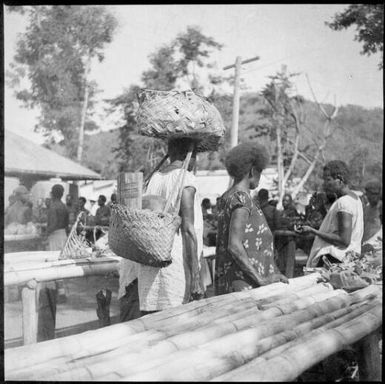 Heavily laden woman, passing between trestle tables, Boong, native market, Rabaul, New Guinea, ca. 1936, 2 / Sarah Chinnery