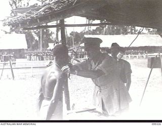 TOROKINA, BOUGAINVILLE, 1945-12-04. MAJOR-GENERAL W. BRIDGEFORD, GENERAL OFFICER IN CHARGE 3 DIVISION, PRESENTING LAIN, A NATIVE SCOUT, WITH A LOYALTY MEDAL, DURING A MEDAL PRESENTATION CEREMONY. ..