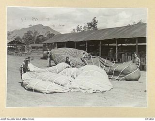 NADZAB, NEW GUINEA. 1944-05-25. MEMBERS OF THE 3RD AIR MAINTENANCE COMPANY EXAMINE FOR FLAWS SALVAGED PARACHUTES WHICH ARE DRYING IN THE SUN. SOME OF THESE BRILLIANTLY COLOURED PARACHUTES ARE MADE ..
