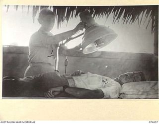 LAE, NEW GUINEA. 1944-07-14. TFX6011 LIEUTENANT T G SECRETAN, PHYSIOTHERAPIST (1) ADJUSTING AN INFRA RED LAMP WHILE TREATING A SKIN RASH ON N242528 LANCE CORPORAL A RYAN IN THE PHYSIOTHERAPHY ..