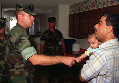 GUNNERY SGT. C. S. Barnum, Tiyan Zone Liaison, Combat Service Support Detachment 37, interacts with a Kurdish baby while he makes his daily rounds to the evacuee community to ensure all of their needs are met