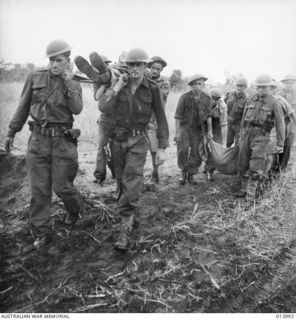 1942-12-05. BUNA. AT AN ADVANCED AMERICAN DRESSING STATION. WOUNDED BEING BROUGHT IN ON STRETCHERS AND IN MAKESHIFT CANVAS CARRIERS, BY SOLDIERS