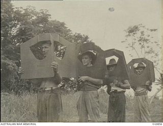 KIRIWINA, TROBRIAND ISLANDS, PAPUA. C. 1943-11. ARMOURERS OF NO. 8 SQUADRON RAAF CARRYING TAILPIECES FOR 2000LB BOMBS OVER THEIR HEADS