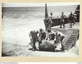 BOUGAINVILLE ISLAND. 1945-03-06. PERSONNEL OF HEADQUARTERS, 7TH INFANTRY BRIGADE ROLLING A 44 GALLON DRUM OFF A BARGE AT TOKO BEACH, THE SITE OF THE NEW UNIT HEADQUARTERS. IDENTIFIED PERSONNEL ARE: ..