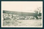 Group of people sitting under an aeroplane watching cricket match, Lae, New Guinea, Mar 1933