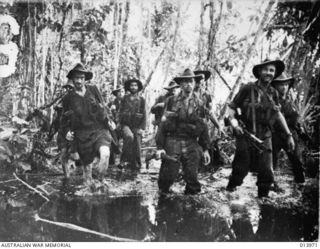 1942-12. PAPUA. BUNA. AUSTRALIAN TROOPS OF 2/7TH CAVALRY REGIMENT AT CAPE ENDAIADERE ADVANCE THROUGH MUD AND SLUSH ON BUNA. FRONT LEFT IS DAVE HERBERT, BEHIND HIM AT FAR REAR IS FRED OUGHTON, ..