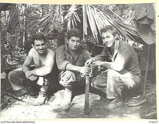 1943-08-30. NEW GUINEA. SITTING IN FRONT OF THEIR ROUGH SHACK MADE OF LEAVES, THREE AMERICANS TAKE ADVANTAGE OF ONE OF THE VERY FEW BURSTS OF SUNSHINE ON MOUNT TAMBU. LEFT TO RIGHT. LT. F.V. ..