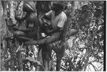 Bridge-building: men sit on frame lashed with vines, one man holds steel axe