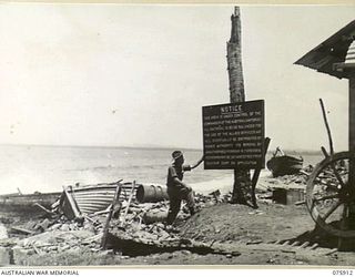 HANSA BAY, NEW GUINEA. 1944-09-06. VX89946 GUNNER H.J. SWIFT, 2/14 FIELD REGIMENT, READING A SIGN AMONG THE WRECKED BOATS ON THE BEACH IN THE AREA CONTROLLED BY THE 5TH DIVISION SALVAGE UNIT