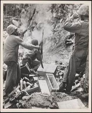 Marine grenadier, with his rifle smoking from the charge, lobs grenades over a ridge into the enemy lines