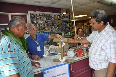 Tafuna, American Samoa, December 14, 2009 -- David Kulberg, FEMA Mitigation Specialist, explains "continuous load path" construction technique to build strong, earthquake and wind-resistant dwellings. Anufe Lavatai, right, and Faitio Faatea, left, customers of C. B. T. Ho Ching & Co. , listen while cashier Tulai Lilomaiava looks on. FEMA/Richard O'Reilly.