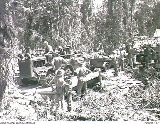 THE SOLOMON ISLANDS, 1945-04-24/27. A TRACTOR ATTEMPTS TO HAUL A LINE OF LADEN TRAILERS ALONG A DIFFICULT ROAD ON BOUGAINVILLE ISLAND WHILE AUSTRALIAN SERVICEMEN STAND BY TO ASSIST AS REQUIRED. ..