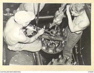 LABU, NEW GUINEA. 1944-10-03. CRAFTSMAN H. KEATES (1) AND CRAFTSMAN J. HUME (2) OF THE 1ST WATERCRAFT WORKSHOPS, USING THEIR MAKESHIFT CYLINDER GRINDING EQUIPMENT TO REGRIND ONE OF THE CYLINDERS OF ..