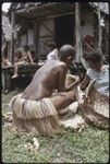 Mortuary ceremony: mourning woman with shaved head arranges banana leaf bundles at exchange