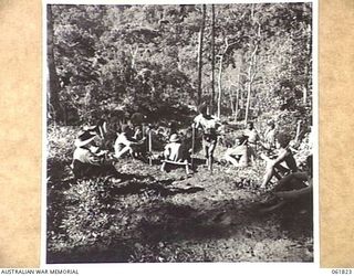 UBERI, NEW GUINEA. 1943-12-19. MEN OF THE 2/9TH AUSTRALIAN INFANTRY BATTALION AND NATIVE CARRIERS ENJOY A REST ALONG THE KOKODA TRAIL IN THE OWEN STANLEY RANGES DURING THE FILMING OF SEQUENCES OF ..