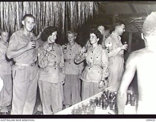 LAE, NEW GUINEA, 1945-12-15. TROOPS AND AUSTRALIAN ARMY MEDICAL WOMEN'S SERVICE GUESTS ENJOYING SOFT DRINKS DURING THE CHRISTMAS DANCE HELD AT AUSTRALIAN NEW GUINEA ADMINISTRATIVE UNIT HEADQUARTERS