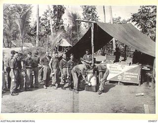 YAMIL SECTOR, NEW GUINEA, 1945-08-01. TROOPS OF 2/6 INFANTRY BATTALION IN LINE FOR THEIR MUG OF COFFEE OR TEA AT THE YMCA CENTRE. MR A.K. HILLIS, YMCA OFFICER IS SEEN POURING IT OUT FOR THE TROOPS