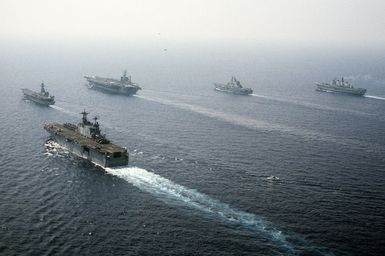 Ships from four nations sail in formation during the NATO Southern Region exercise Dragon Hammer '90. In the left foreground is the amphibious assault ship USS SAIPAN (LHA-2). In the background are, from left: the Spanish aircraft carrier SPS PRINCIPE DE ASTURIAS (R-11), the nuclear-powered aircraft carrier USS DWIGHT D. EISENHOWER (CVN-69), the Italian light aircraft carrier ITS GIUSEPPE GARIBALDI (C-551) and the British light aircraft carrier HMS INVINCIBLE (R-05)