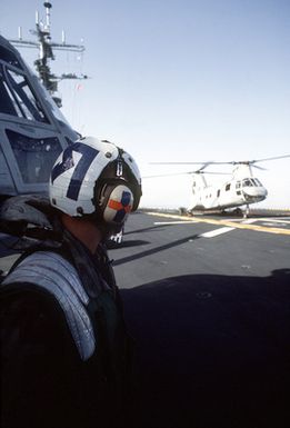 A flight deck crewmen watches as a Marine Medium Helicopter Squadron 261 (HMM-261) CH-46E Sea Knight helicopter is prepared for take off from the amphibious assault ship USS GUAM (LPH-9) during morning physical training (PT)