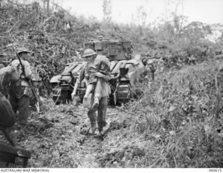 SATTELBERG AREA, NEW GUINEA. 1943-11-17. WOUNDED SOLDIER OF THE 2/48TH. AUSTRALIAN INFANTRY BATTALION BEING CARRIED BACK TO THE ADVANCED DRESSING STATION WHILE TANKS AND INFANTRY CAN BE SEEN MOVING ..