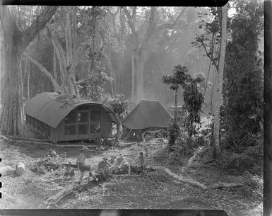 Group of unidentified men sitting in a forest area, at RNZAF (Royal New Zealand Air Force) camp, Guadalcanal, Solomon Islands