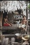 Man and boy sit on house veranda, kitchen equipment on shelves in background