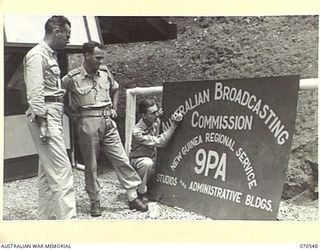 PORT MORESBY, PAPUA, 1944-02-20. CORPORAL E. HUGHES (3), ANNOUNCER, (UNITED STATES STAFF) AND SIGNWRITER PUTTING FINISHING TOUCHES ON A SIGNBOARD TO BE PLACED OUTSIDE THE NEWLY OPENED AUSTRALIAN ..