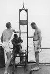 Walter H. Munk (right) and two men lower camera into the water near Palmerston Island