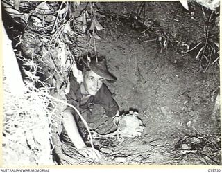 1943-09-15. NEW GUINEA. HODGES KNOLL. AFTER THE JAPANESE HAD BEEN DRIVEN FROM THIS FOX HOLE AT HODGES KNOLL, NEAR KOMIATUM PTE. JOE THOMAS, OF PERTH, FOUND THIS JAPANESE WATERBOTTLE. (NEGATIVE BY ..