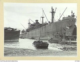 LAE, NEW GUINEA. 1944-03-23. UNITED STATES LIBERTY SHIPS AT HEADQUARTERS LAE BASE SUB-AREA UNLOADING IN THE BACKGROUND. AN AMPHIBIOUS DUKW, ENTERS WATER IN THE FOREGROUND ALONG "DUKW WAY"