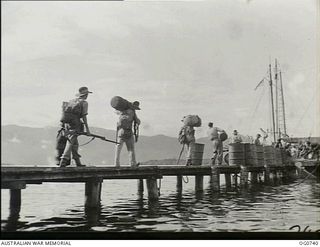 MILNE BAY, PAPUA. C.1944-02. AIRMEN OF NO. 75 SQUADRON RAAF, LOADED WITH THEIR GEAR, WALKING ALONG THE JETTY AT MILNE BAY BEFORE GOING ABOARD SHIP EN ROUTE TO LAE