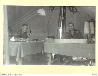 MADANG, NEW GUINEA. 1944-07-22. NX112671 CAPTAIN C.W. POWDITCH G111 OPERATIONS (LEFT) AND VX74779 CAPTAIN C.C. GUY G111 INTELLIGENCE (RIGHT) IN THEIR TENT OFFICE AT HEADQUARTERS, 5TH DIVISION