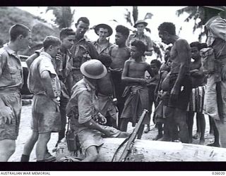 PAPUA, NEW GUINEA, 1942-07. AUSTRALIANS ON PATROL THROUGH A COASTAL SECTION OF NEW GUINEA STOP AT A NATIVE VILLAGE TO BARTER FOR COCONUTS, BANANAS AND NATIVE CURIOS. TRADE IS GENERALLY VERY KEEN ..