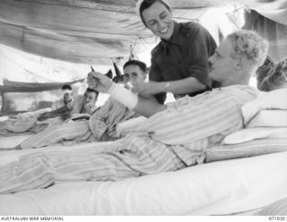 HELDSBACH MISSION, FINSCHHAFEN ARE, NEW GUINEA. 1944-03-13. NFX70245 SISTER N.G. LUKE, OF THE AUSTRALIAN ARMY NURSING SERVICE (AANS), BANDAGES THE WOUND OF VX104799 PRIVATE G.K. ABSON IN A TENT ..