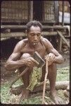 Canoe-building: Gisigesi uses axe to smooth a piece of wood for outrigger frame, he smokes