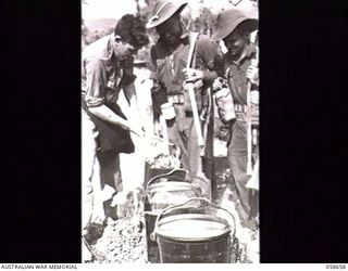 RAMU VALLEY, NEW GUINEA. 1943-10-06. NX28693 SAPPER H. GLANVILLE, COOK OF THE 2/6TH AUSTRALIAN FIELD COMPANY, ROYAL AUSTRALIAN ENGINEERS, PREPARING A MEAL FOR TWO HUNGRY AND IMPATIENT SAPPERS, ..