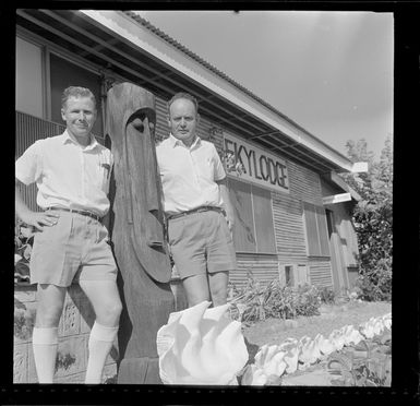 Two unidentified men standing next to a carved wooden sculpture outside the Skylodge Hotel, Nadi, Fiji