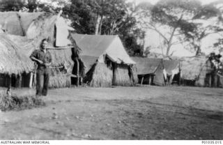 GUSAP RIVER REGION, NEW GUINEA, C. 1943. LIEUTENANT BRIAN HOPKINS, OFFICER-IN-CHARGE OF GUSAP SUB-SECTOR, STANDING OUTSIDE THE HUTS USED AS HEADQUARTERS FOR THE GUSAP SPOTTERS IN THE NEW GUINEA AIR ..