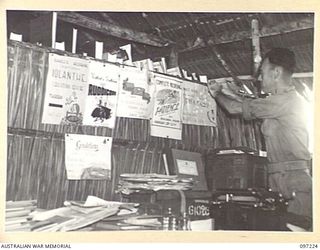 CAPE WOM, NEW GUINEA. 1945-09-29. WARRANT OFFICER 1 G.J. WHITE AT HEADQUARTERS 6 DIVISION WITH POSTERS MADE BY THE AUSTRALIAN ARMY EDUCATION SERVICE TO ADVERTISE THE "MUSIC AND LECTURE NIGHTS"