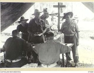 ALEXISHAFEN, NEW GUINEA. 1944-05-27. TROOPS FROM HEADQUARTERS 8TH INFANTRY BRIGADE OUTSIDE A TENT COVERED POLLING BOOTH TO RECORD THEIR VOTES IN THE NEW SOUTH WALES STATE ELECTIONS. IDENTIFIED ..