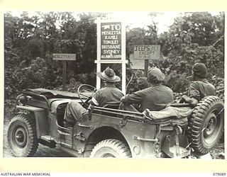 BOUGAINVILLE ISLAND. 1945-02-12. TROOPS OF HEADQUARTERS, 7TH INFANTRY BRIGADE PAUSE TO READ A NEW ROAD SIGN AT MAWARAKA ON THE MOSIGETTA ROAD