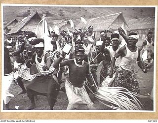 KILA KILA, PAPUA, NEW GUINEA. 1943-12-25. KEREMA BOYS EXECUTING A DANCE AT THE AUSTRALIAN AND NEW GUINEA ADMINISTRATION UNIT NATIVE LABOUR CAMP. THE DANCERS WEAR LONG TRAILS OF GRASS AND FLOWERS, ..