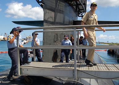 US Navy (USN) ENSIGN (ESN) Ted Doukas, assigned to the USN Los Angeles Class Attack Submarine USS HOUSTON (SSN 713), leads group of Sea Cadets and visitors back across the brow following a tour of the boat. The group of 18 cadets toured the submarine to learn more about life in the Navy. The USS HOUSTON is currently deployed at Apra Harbor, Guam and regularly deploys throughout the Pacific region to support 7th Fleet operations