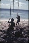 Children swing on vines at a beach on Kiriwina near Kaibola village