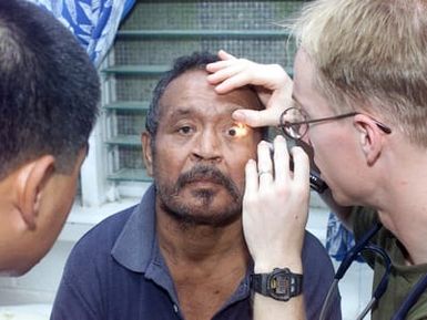 Navy Lieutenant Adam Pacal, a flight surgeon from HMH-463, checks into the eyes of Kikuwo Kodeb, a diabetes patient in Peleliu in a community relations project during Exercise KOA THUNDER 2001. KOA THUNDER is an exercise involving elements of 1ST Marine Air Wing (MAW), and 3rd Marine Division, where Marines conduct an Operational Readiness Exercise (ORE). The Aviation Support Element (ASE) from Kaneohe Bay, Hawaii, will be tested on command and control of several different missions, to include Tactical Recovery of Aircraft and Personal (TRAP), airfield seizures, and a Noncombatant Evacuation Operation (NEO)