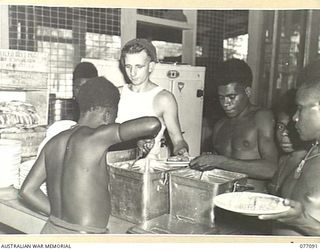 LAE AREA, NEW GUINEA. 1944-11-26. VX132456 PRIVATE W.A. PACKWOOD, DISHING UP DINNER FOR THE WAITING AUSTRALIAN NEW GUINEA ADMINISTRATIVE UNIT NATIVE WAITERS AT THE 22ND ARMY CANTEEN SERVICES OTHER ..