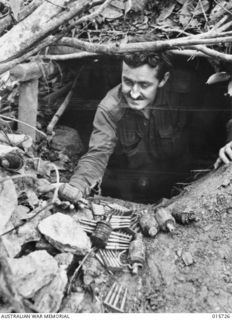 1943-09-15. NEW GUINEA. HODGES KNOLL. AFTER THE JAPANESE HAD BEEN DRIVEN FROM THIS FOX HOLE AT HODGES KNOLL NEAR KOMIATUM, PTE. KEAN, OF SWAN HILL, VIC., FOUND THESE JAPANESE GRENADES AND SMALL ..