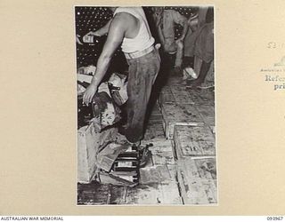 PALMALMAL PLANTATION, JACQUINOT BAY, NEW BRITAIN, 1945-07-10. PERSONNEL OF AUSTRALIAN ARMY CANTEEN SERVICE, ATTACHED 5 BASE SUB-AREA, HANDLING SOME OF THE BROKEN BOTTLES AND CARTONS IN THE BULK ..