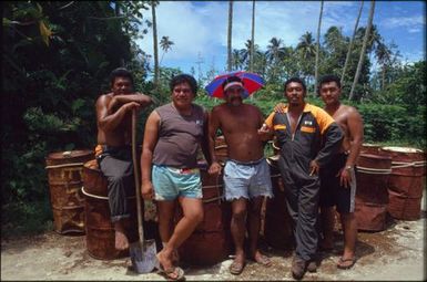 Group of men standing by oil drums, Mauke